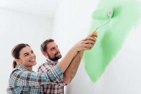 Young loving couple renovating their home, they are painting walls and holding a paint roller together